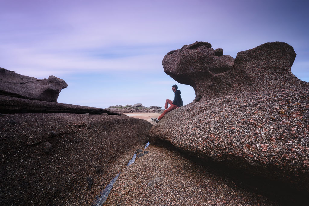 Homme sous un rocher granitique en bord de mer