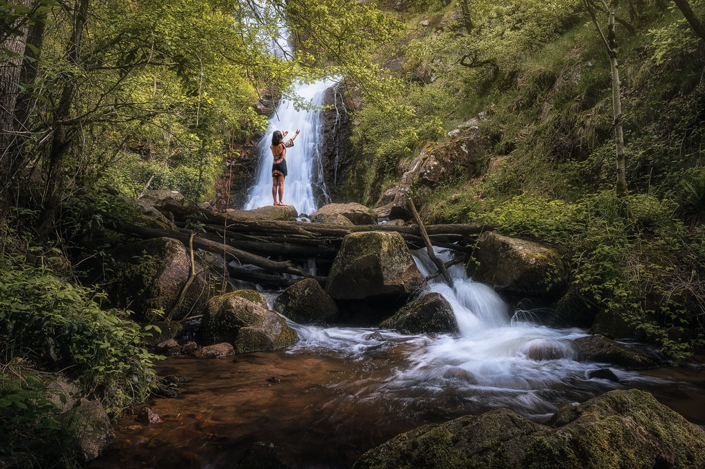 Femme levant les bras au ciel sur fond de cascade