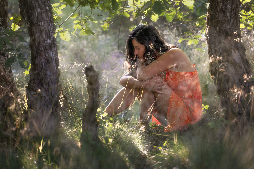 Femme songeuse assise sous les arbres.